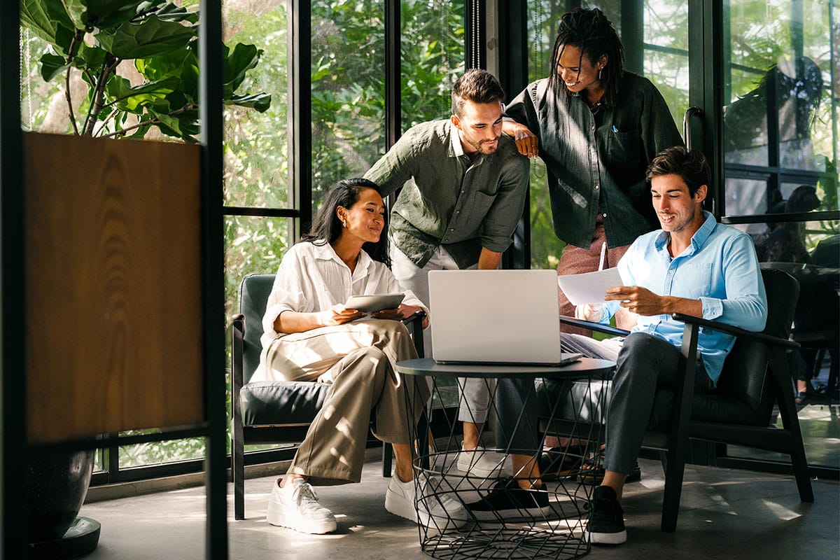 Une équipe d’experts collaborant autour d'un ordinateur portable et de documents dans un espace de travail lumineux et moderne rempli de plantes.