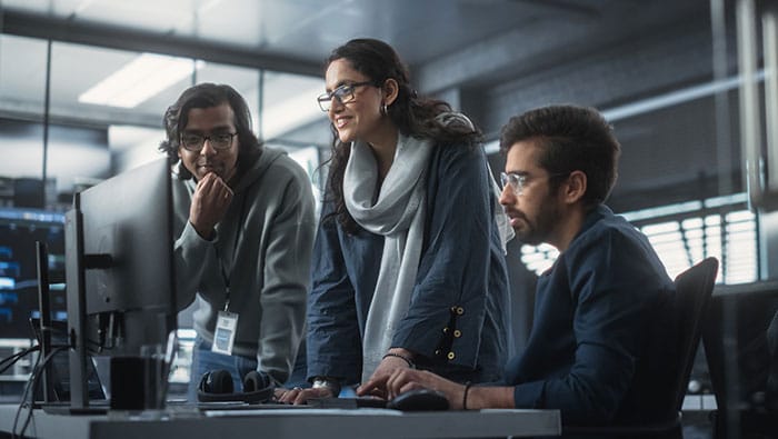 Trois développeurs travaillent ensemble autour d'un ordinateur pour concevoir une solution IdO et accéder à la documentation technique via le Centre des développeurs de Bell.