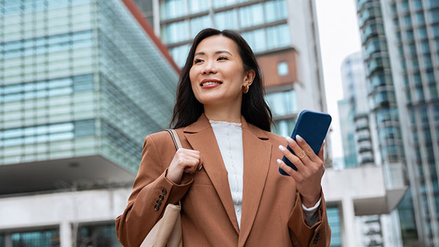 Professionnelle souriante utilisant son téléphone intelligent, mettant en valeur les forfaits de mobilité d'entreprise flexibles de Bell pour les équipes.