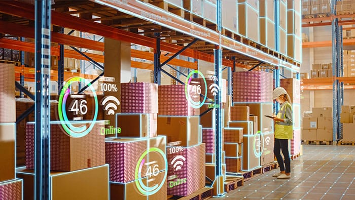 Une personne qui travaille dans un entrepôt utilise une tablette pour balayer et gérer les stocks, avec des icônes numériques montrant les données recueillies dans les boîtes.