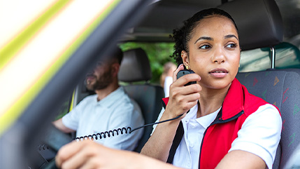 Dans un véhicule d’urgence, une intervenante de sécurité publique utilise une radio portative. Ceci illustre les solutions de sécurité publique de Bell, dont le système radio P25, les technologies de RAO et des applications réseau critiques qui offrent une communication fiable en tout temps.