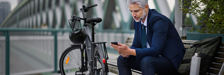 A man sitting next to his bicycle looking at his Snik bike security app on his phone.