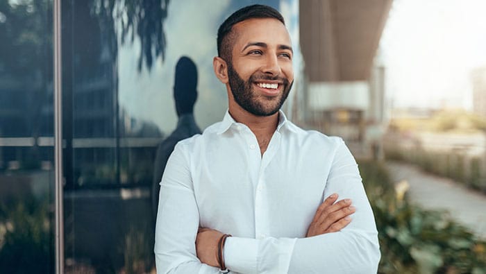 Une professionnelle des affaires souriante se tient avec assurance devant un bâtiment moderne en verre, représentant la découverte de perspectives de l'IdO pour les cadres et les tendances de transformation d'entreprise.