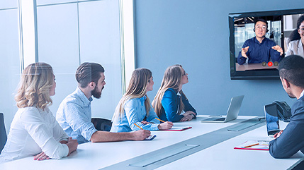 Des collègues assistent à une réunion autour d’une table de conférence et communiquent avec des travailleurs à distance lors d’un appel vidéo au moyen d’une solution vocale et de collaboration de Bell.